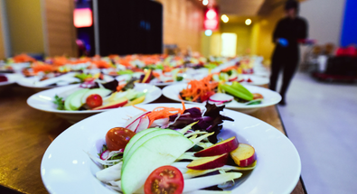 A close-up of a plated salad with long rows of identical plates behind it, illustrating proper catering portion sizes for a guide to Calgary events.